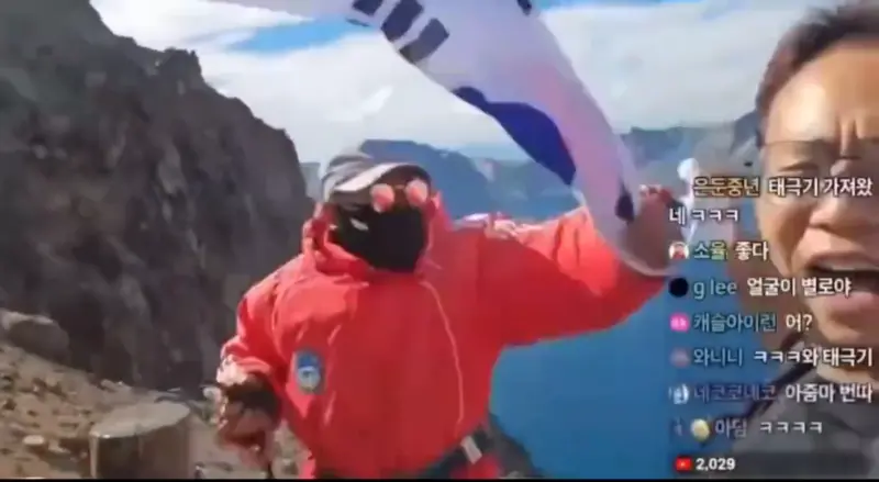 ▲韓國一名網紅日前到中國東北旅遊,在登上長白山時,拿出韓國國旗揮舞還唱韓國國歌,隨即一旁工作人員就沖上前搶走國旗。(圖/翻攝自微博)