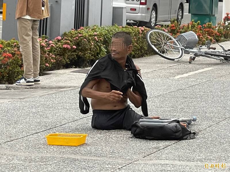 打赤膊趴地乞讨的男子，熬不住水泥地高温爬起身穿衣。（记者黄良杰摄）