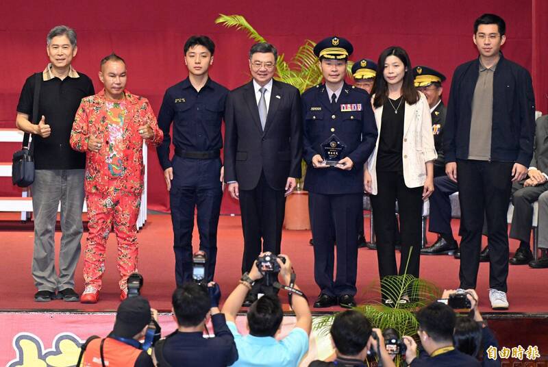 行政院长卓荣泰（中）22日出席台湾警察专科学校庆祝80周年校庆大会，颁奖给杰出校友时，竹北「吊车大王」胡汉䶮（左二）以获奖人亲友身分上台合影，引起全场瞩目。（记者廖振辉摄）