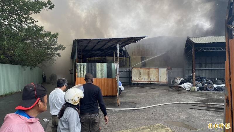 桃园区树仁三街网拍仓库火灾有扩散到后方废车辆与废轮胎回收场之虞，消防单位增设水线降温隔热，回收场奈及利亚裔张姓男负责人（黑衣者）很是焦急。（记者陈璟民摄）