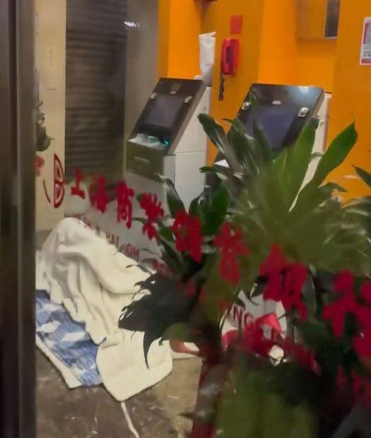 有人霸占台北市信义路四段上海商银松南分行的自动柜员机服务区，反锁玻璃门铺上被褥盖著棉被呼呼大睡，引起网友热议。（图撷取自网路影片）